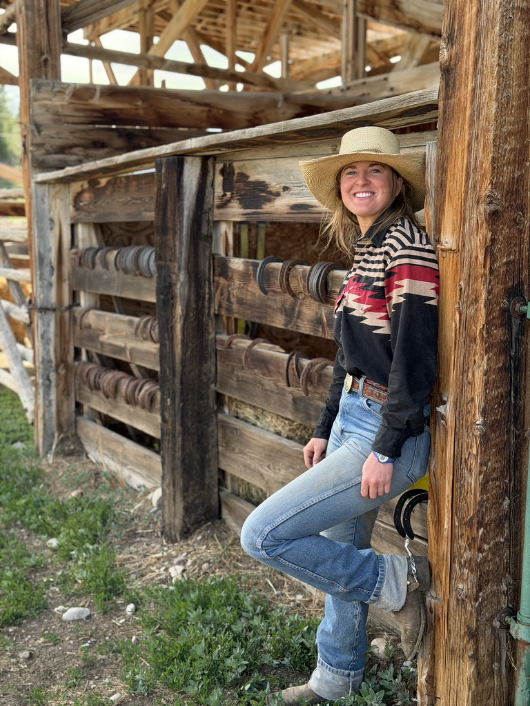 Faith Hamlin wearing a hat and leaning against a wooden barn