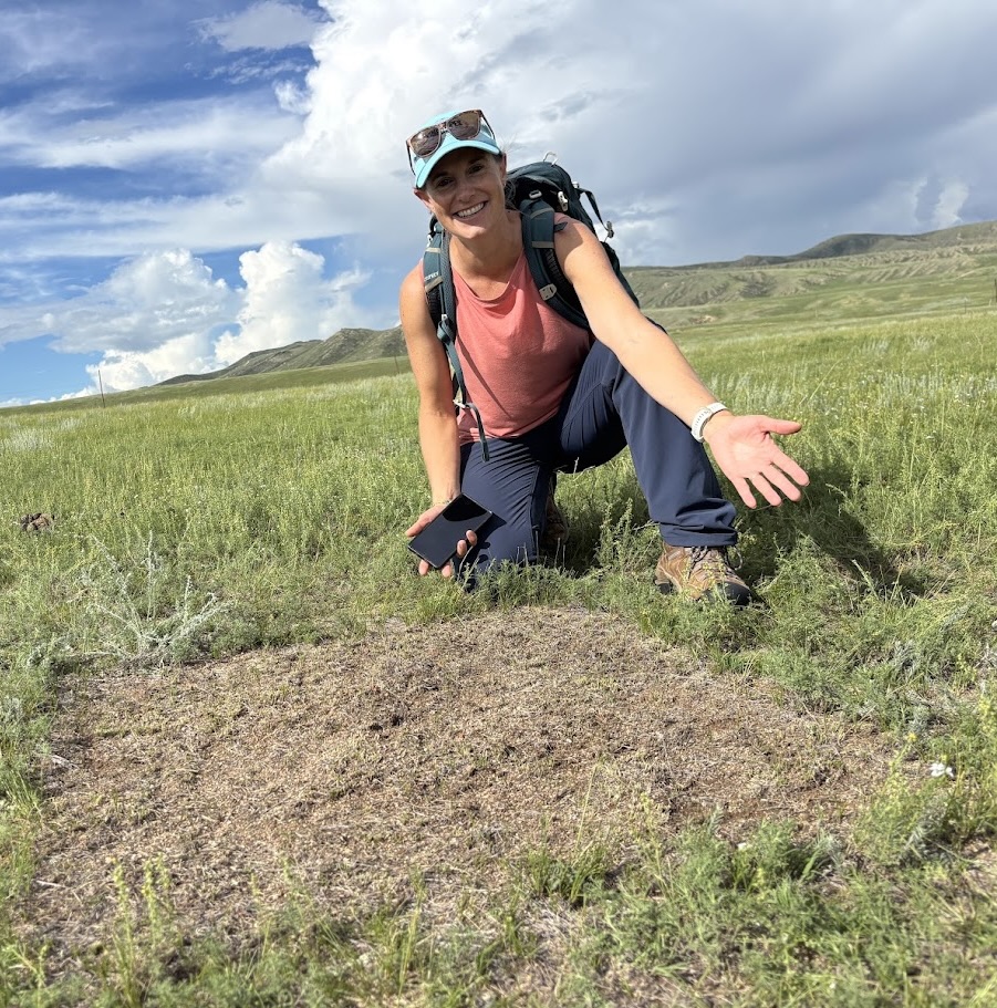 Mae Smith kneeling in a rangeland landscape