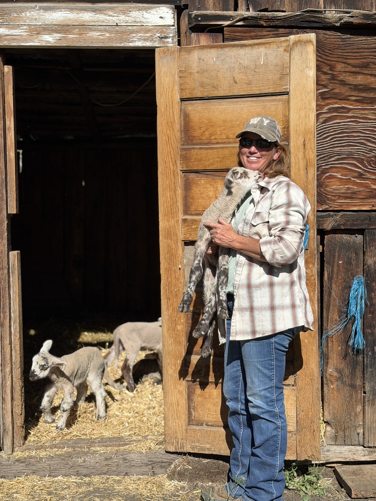Trudi Julian holding a lamb outside a ranch building